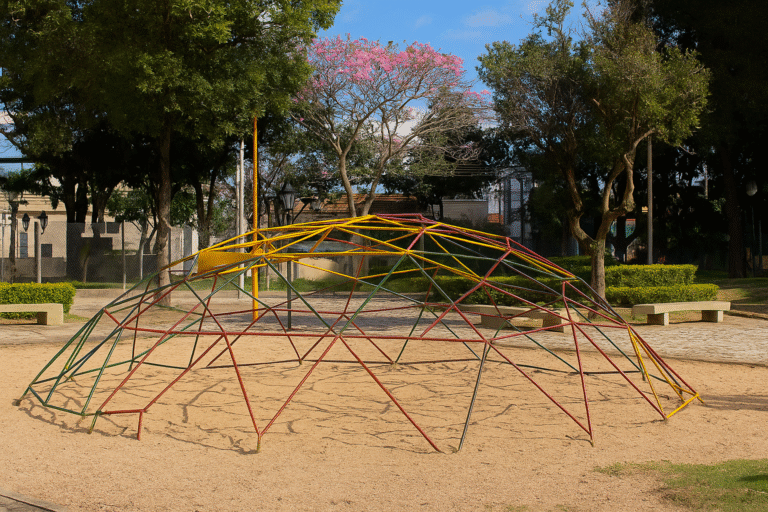 Parquinho infantil com estrutura de escalada em formato de cúpula, rodeado por árvores e bancos em uma praça de Indaiatuba.