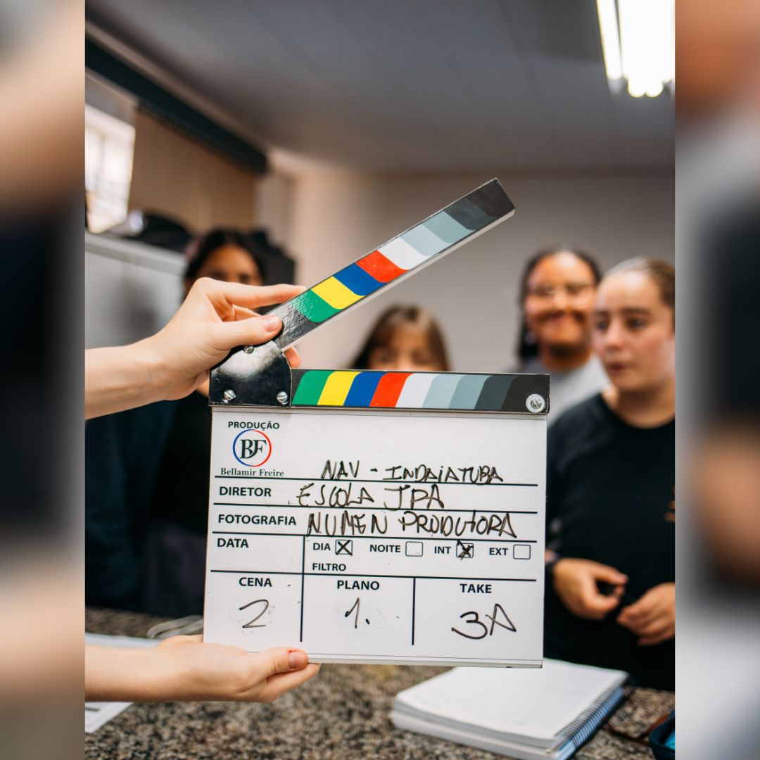 Foto de um grupo de jovens ao fundo e em primeiro plano uma claquete ilustrando o inicio das oficinas do projeto nucleo audiovisual em Indaiatuba