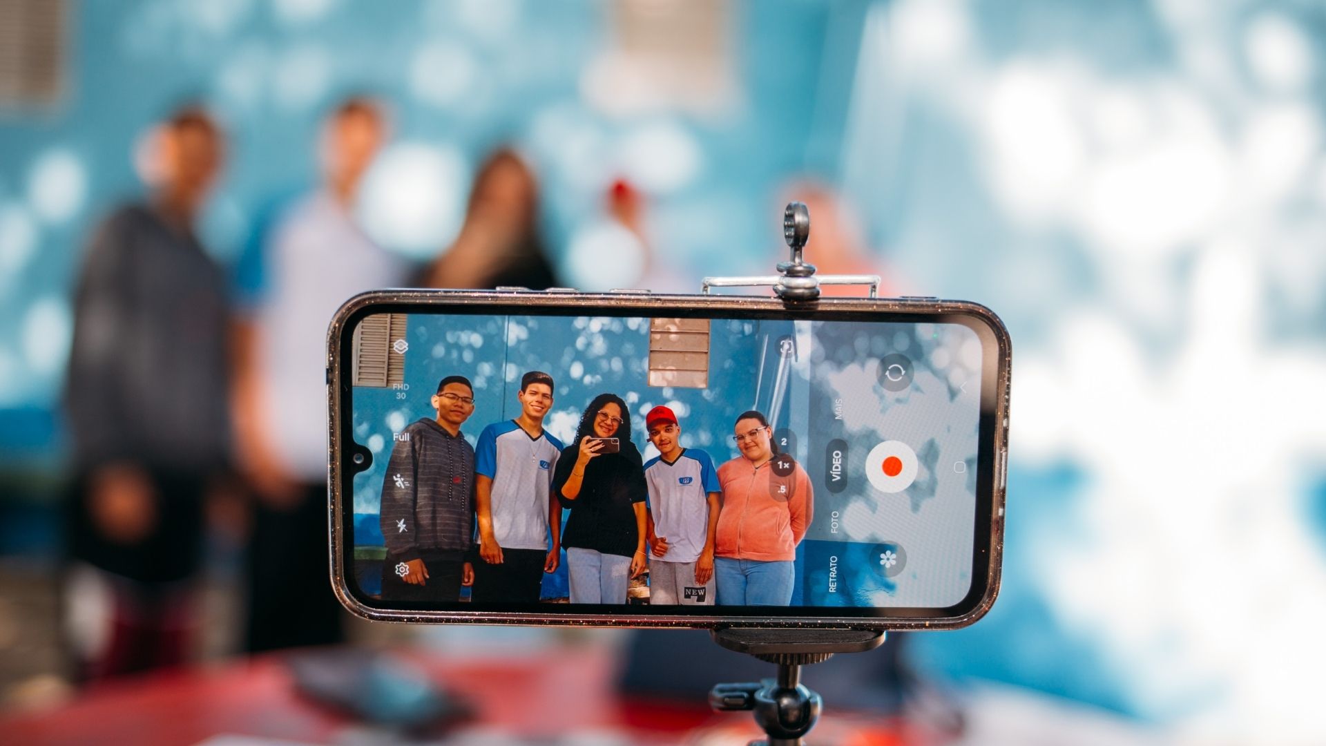 Fotografia mostrando a tela de um celular gravando um grupo de jovens em uma sala de oficina do Projeto Núcleo Audiovisual Indaiatuba